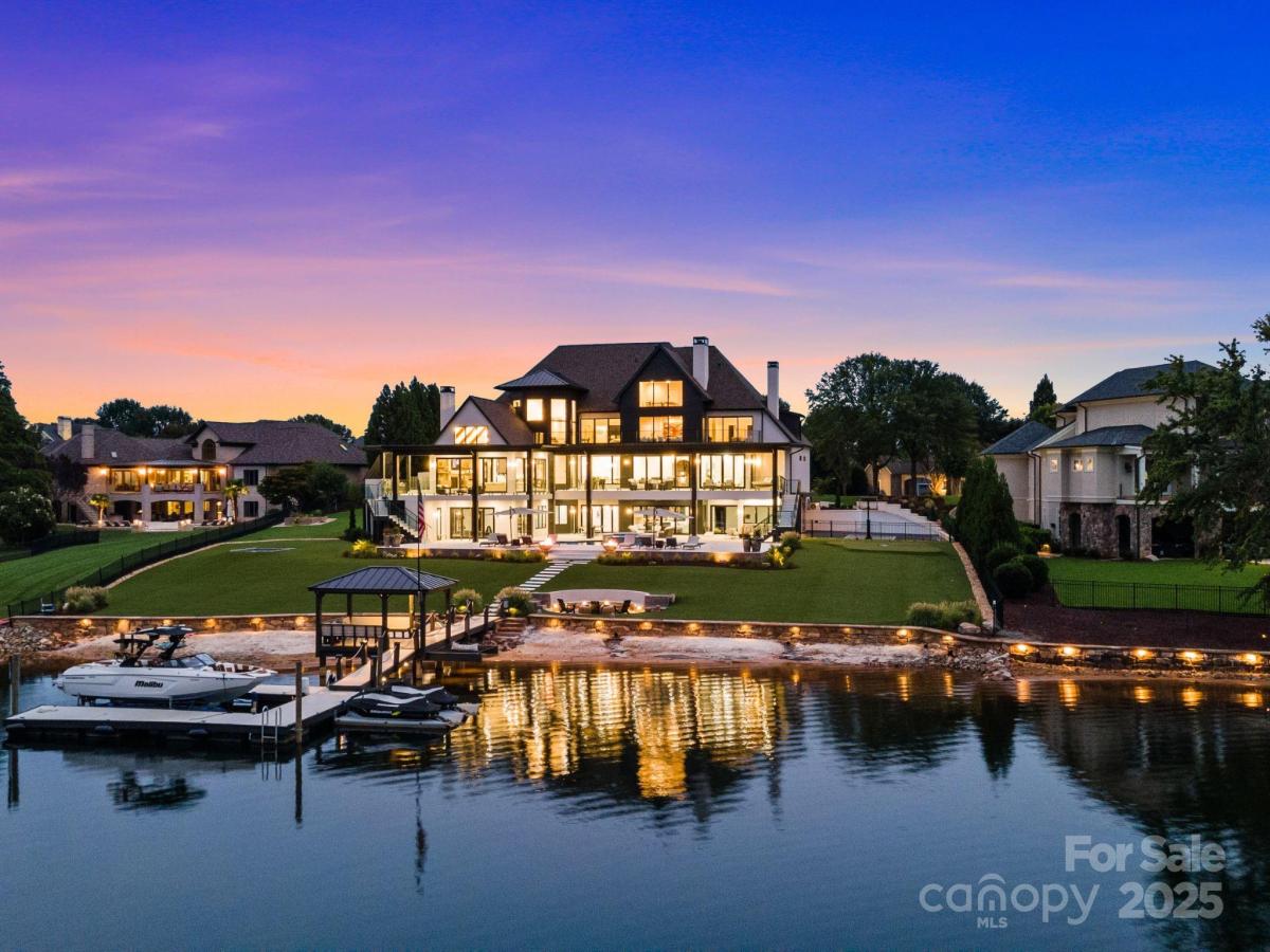 A luxury home by the lake at dusk, illuminated by soft lights reflecting on the water's surface.